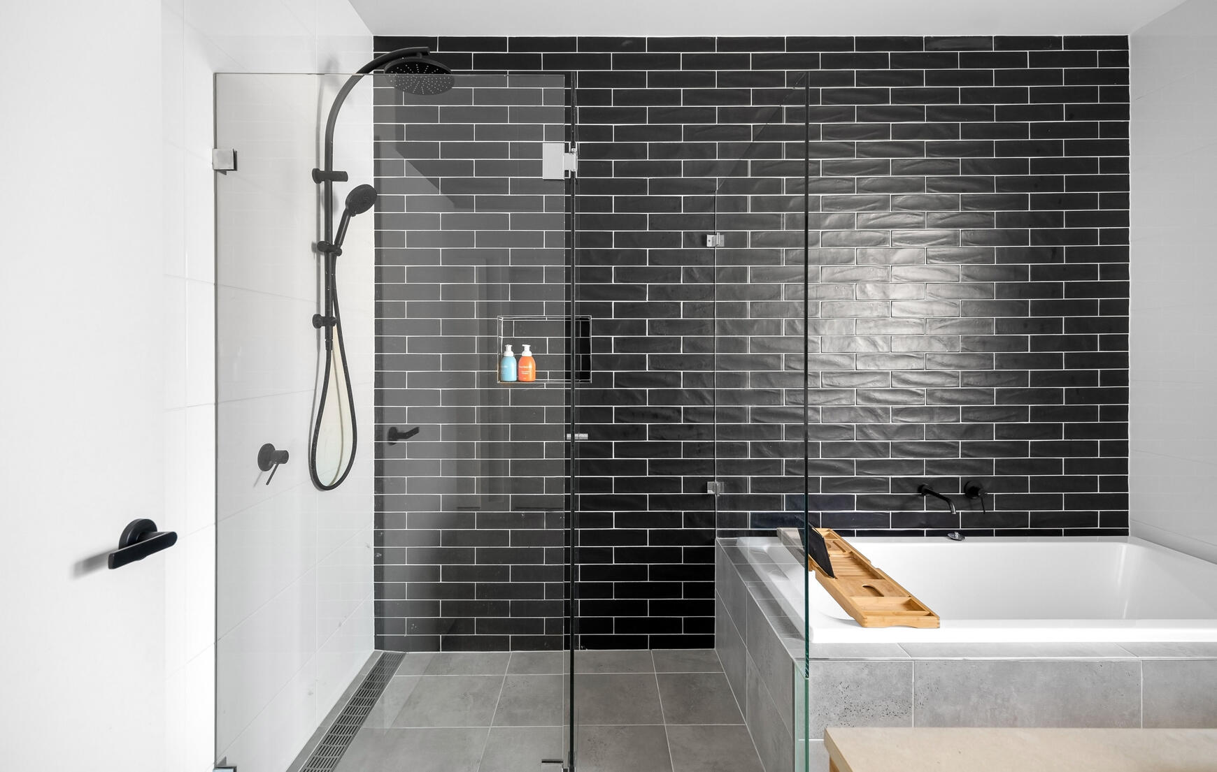 Sydney Bathroom Renovation with Black Subway Tile Feature Wall Sydney bathroom renovation with black subway tile feature wall, black fittings, white 300x600mm porcelain wall tiles, white bath, frameless shower screen and grey marble-look 300x300mm porcelain floor tiles